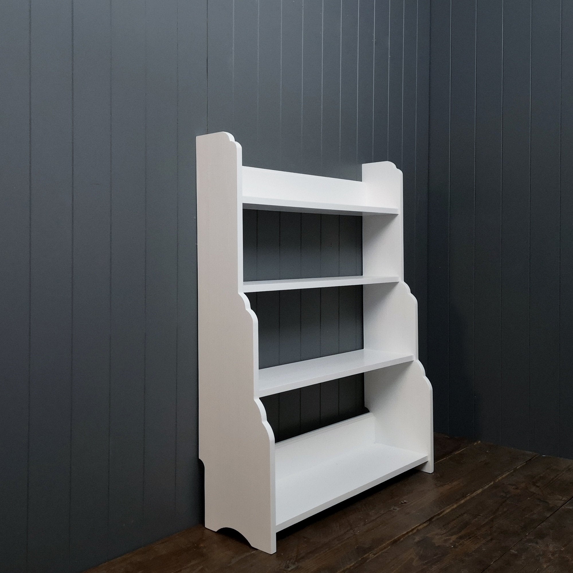 A solid wooden bookcase painted white with 4 shelves of different depths. Smallest at the top to deepest at the bottom.